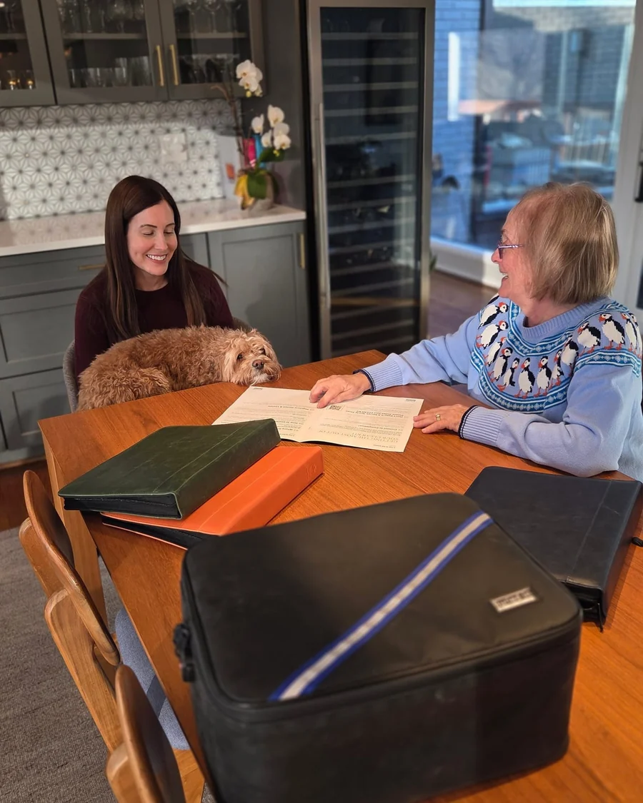 A mother and daughter at a kitchen table going through an estate document together, with the CLEAR Kit binders and its fire resistant case in front of them